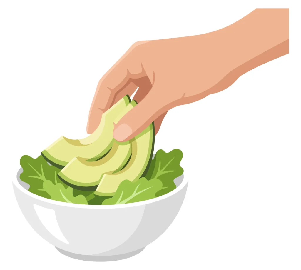 A hand adds avocado slices to a bowl of lettuce leaves